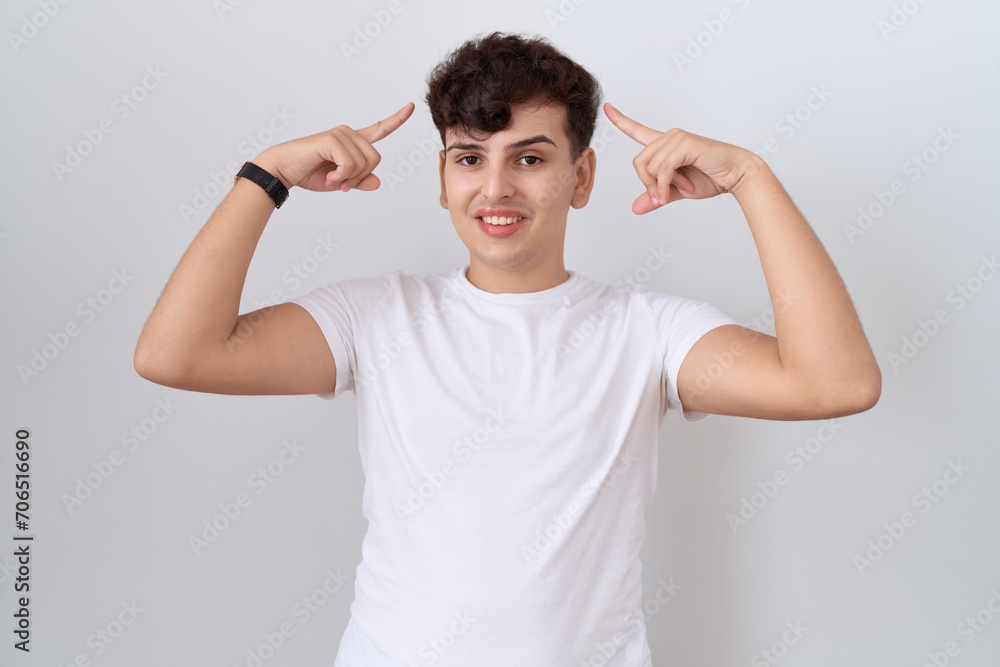 Young non binary man wearing casual white t shirt smiling pointing to head with both hands finger, great idea or thought, good memory Young non binary man wearing casual white t shirt smiling pointing to head with both hands finger, great idea or thought, good memory