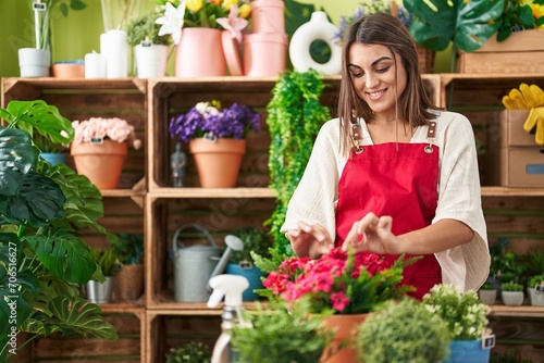 Young beautiful hispanic woman florist smiling confident touching plant at flower shop