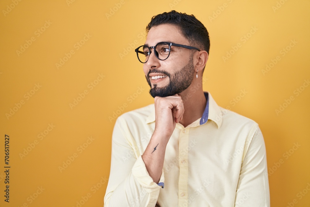 Hispanic young man wearing business clothes and glasses with hand on chin thinking about question, pensive expression. smiling and thoughtful face. doubt concept. Hispanic young man wearing business clothes and glasses with hand on chin thinking about question, pensive expression. smiling and thoughtful face. doubt concept.