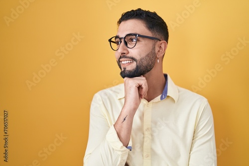Hispanic young man wearing business clothes and glasses with hand on chin thinking about question, pensive expression. smiling and thoughtful face. doubt concept.