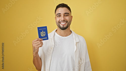Smiling young man holding cuban passport against yellow background
