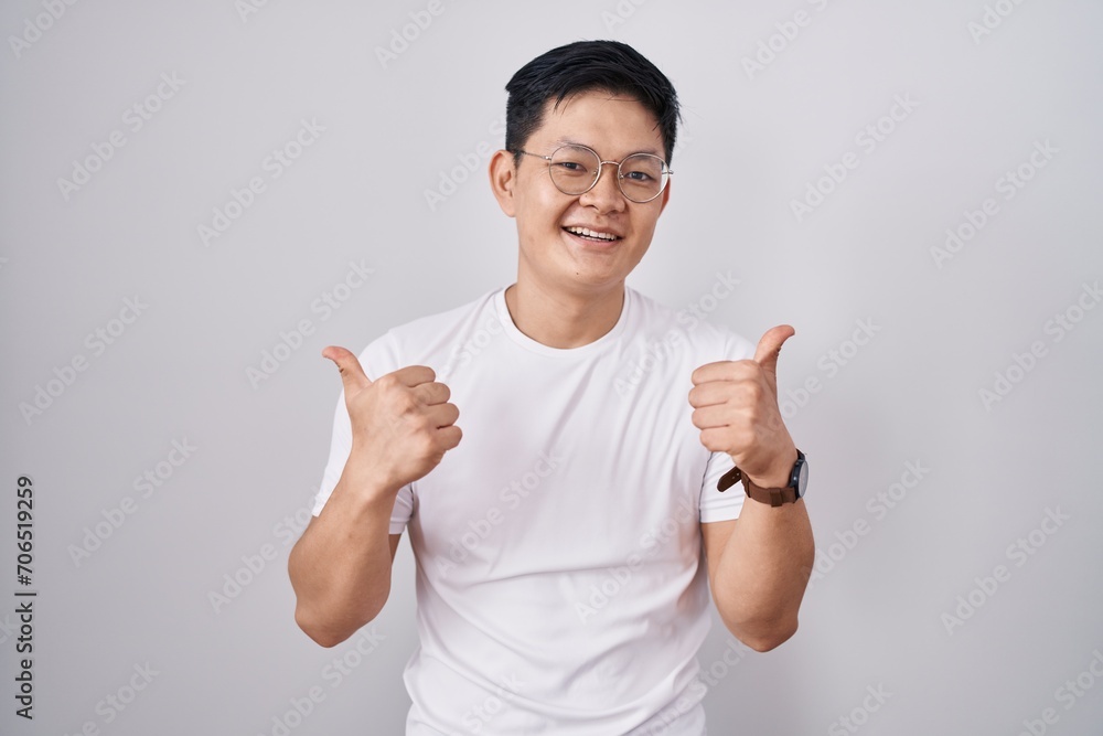 Young asian man standing over white background success sign doing positive gesture with hand, thumbs up smiling and happy. cheerful expression and winner gesture. Young asian man standing over white background success sign doing positive gesture with hand, thumbs up smiling and happy. cheerful expression and winner gesture.