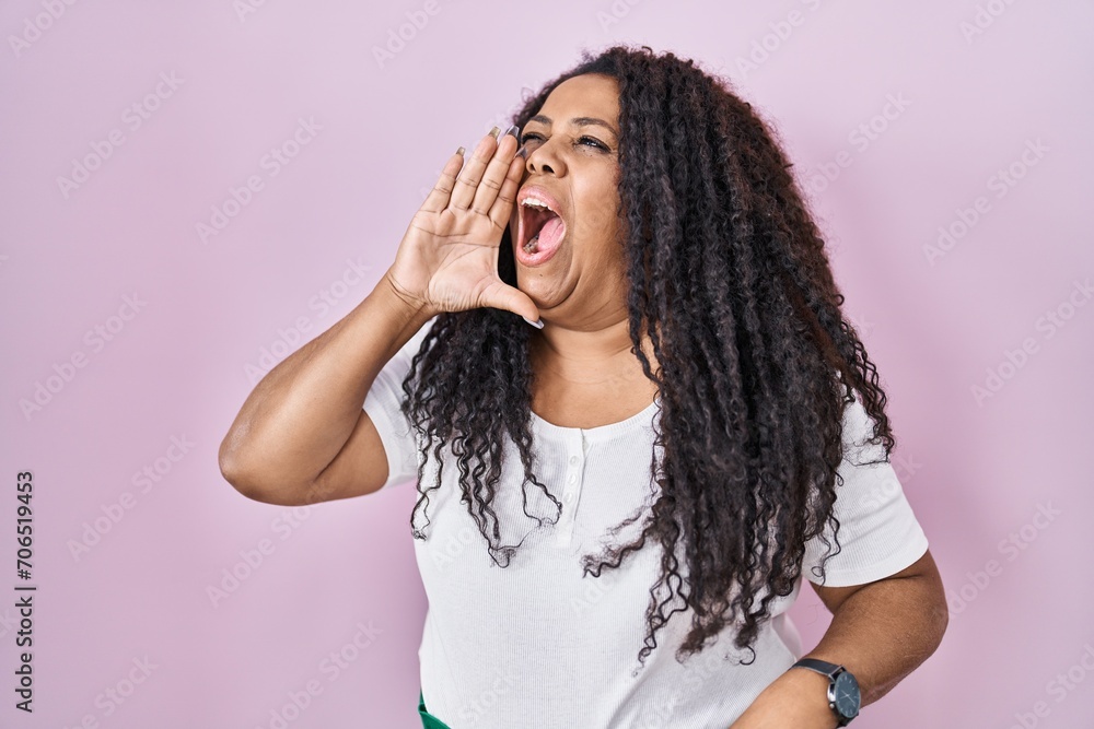 Plus size hispanic woman standing over pink background shouting and screaming loud to side with hand on mouth. communication concept. Plus size hispanic woman standing over pink background shouting and screaming loud to side with hand on mouth. communication concept.