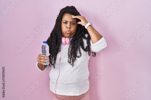 Plus size hispanic woman wearing sportswear and headphones worried and stressed about a problem with hand on forehead, nervous and anxious for crisis