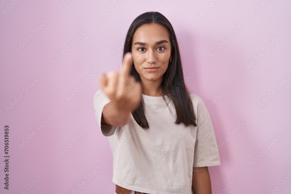 Young hispanic woman standing over pink background showing middle finger, impolite and rude fuck off expression Young hispanic woman standing over pink background showing middle finger, impolite and rude fuck off expression