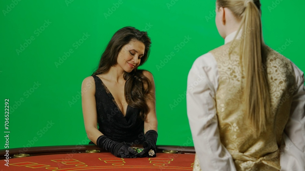 Elegant female in studio on chroma key green screen. Attractive woman in black dress and croupier at the blackjack poker table takes winning chips Elegant female in studio on chroma key green screen. Attractive woman in black dress and croupier at the blackjack poker table takes winning chips