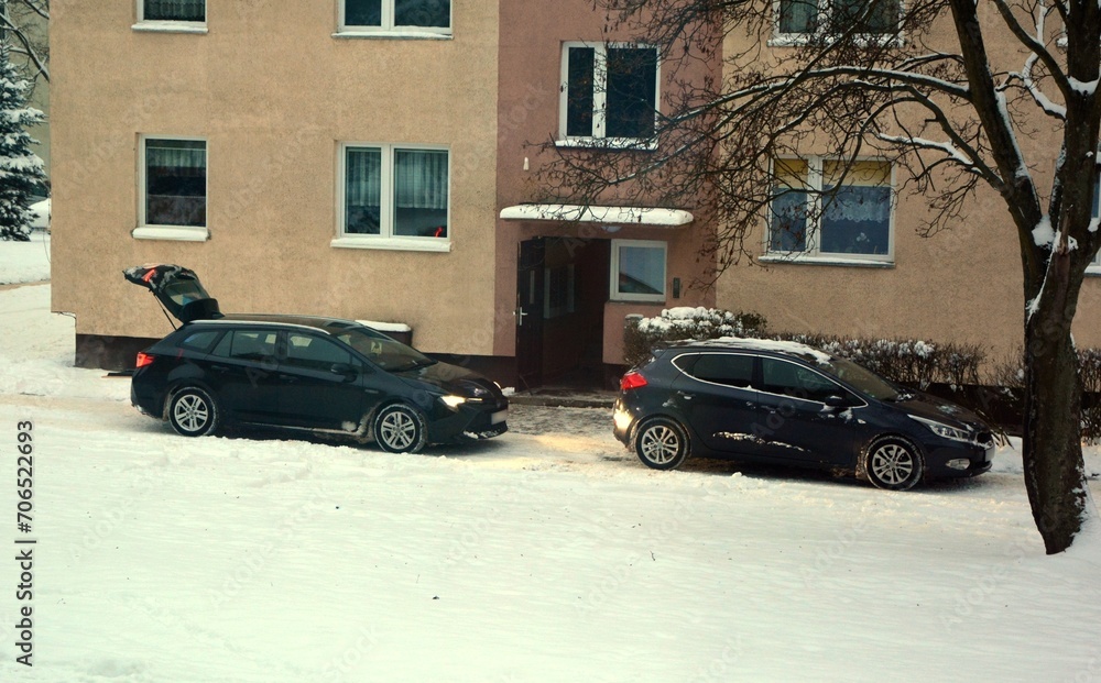 Two cars by an apartment block in winter overlooking the snow