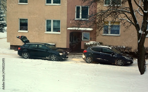 Two cars by an apartment block in winter overlooking the snow