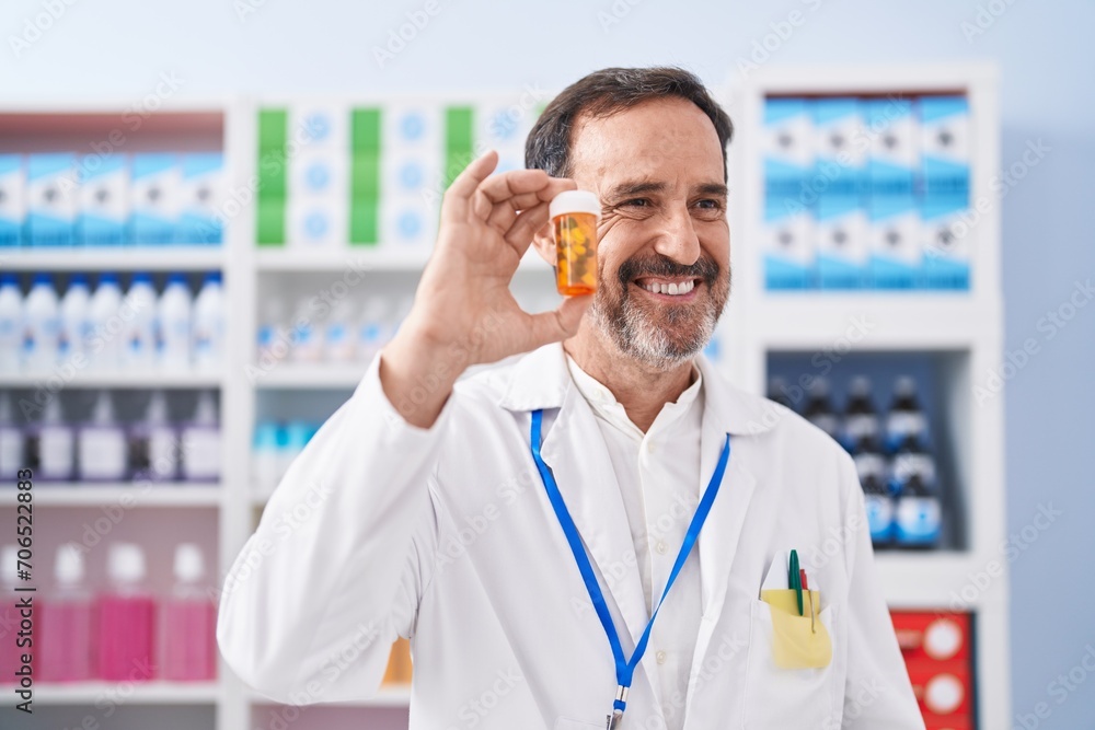 Middle age man pharmacist smiling confident holding pills bottle at pharmacy Middle age man pharmacist smiling confident holding pills bottle at pharmacy
