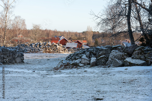 Typical landscape in Sweden in winter time. In the foreground are large boulders that have been cleared from the fields, in the background the village