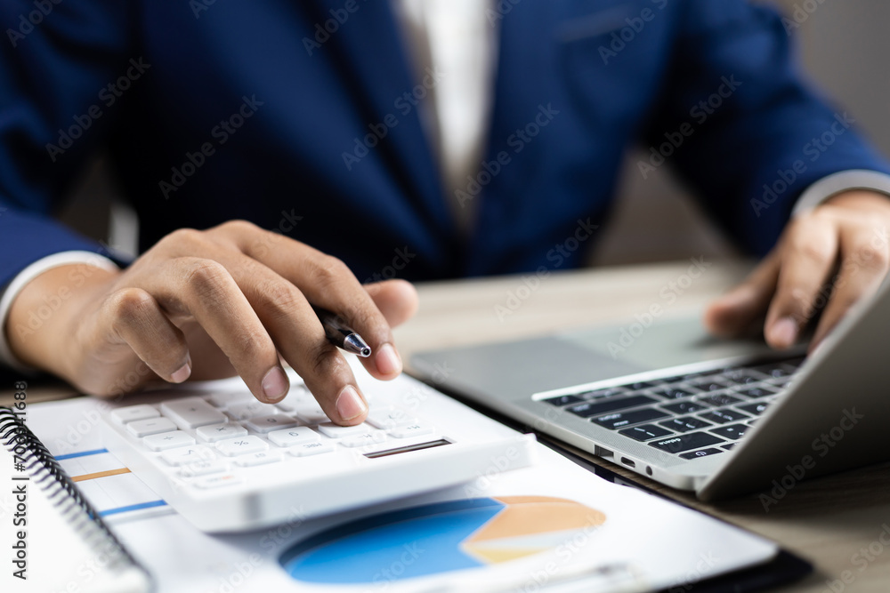 Businessman calculating taxes and finances on laptop at corporate desk, Financial success, Accountant working with calculator and paperwork ,Economy concept. Man managing budget and market statistics. Businessman calculating taxes and finances on laptop at corporate desk, Financial success, Accountant working with calculator and paperwork ,Economy concept. Man managing budget and market statistics.