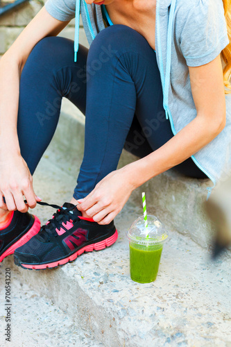 Green detox smoothie cup and woman lacing running shoes before workout