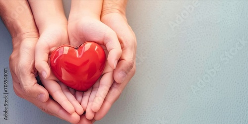 Hands of mother and daughter holding a red heart on a wooden background