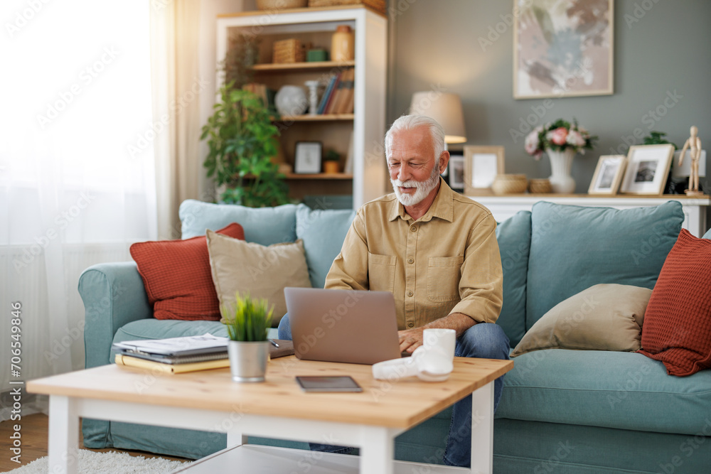Senior man in casual clothing using laptop and smiling while working from home office Senior man in casual clothing using laptop and smiling while working from home office