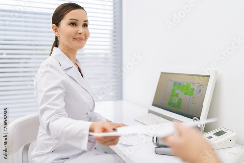 Portrait of friendly female doctor giving prescription paper to unrecognizable patient at checkup appointment. Physician handing out document for treatment and medicine against disease.