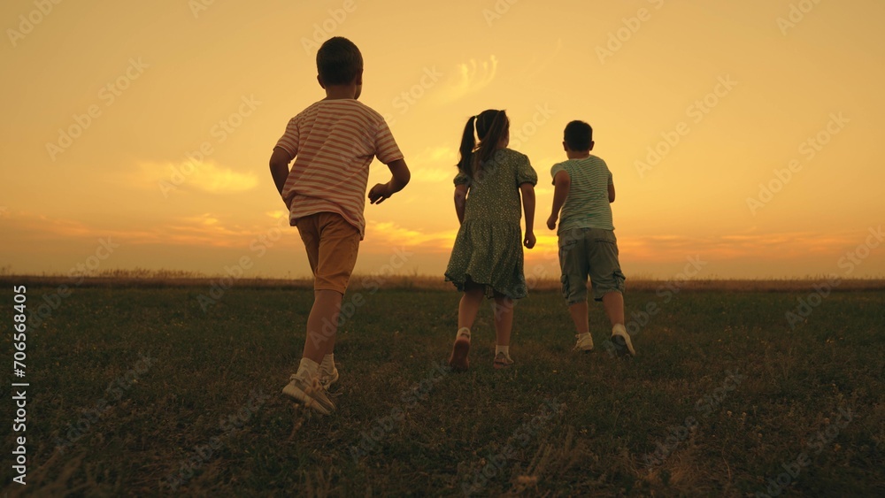Joyful group of children runs together across wild grassy field at sunset light. Happy sister engages in ready steady go game with brothers in summer evening. Positive memories of carefree childhood