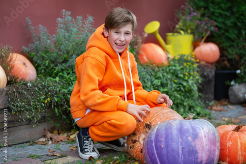 A teenage boy in orange clothes sits near Halloween pumpkins.