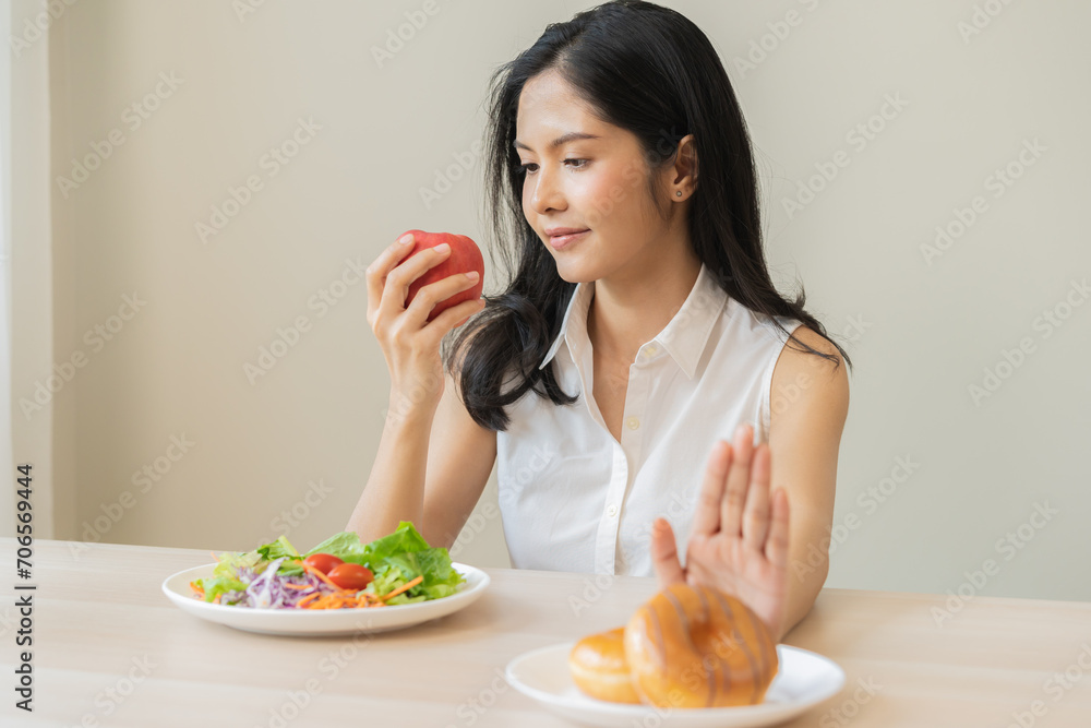 Diet, dieting, happy asian young woman, girl hand push out, deny sweet donut, doughnut on plate, choose red apple and green vegetable salad, eat food for good healthy, female getting weight loss. Diet, dieting, happy asian young woman, girl hand push out, deny sweet donut, doughnut on plate, choose red apple and green vegetable salad, eat food for good healthy, female getting weight loss.