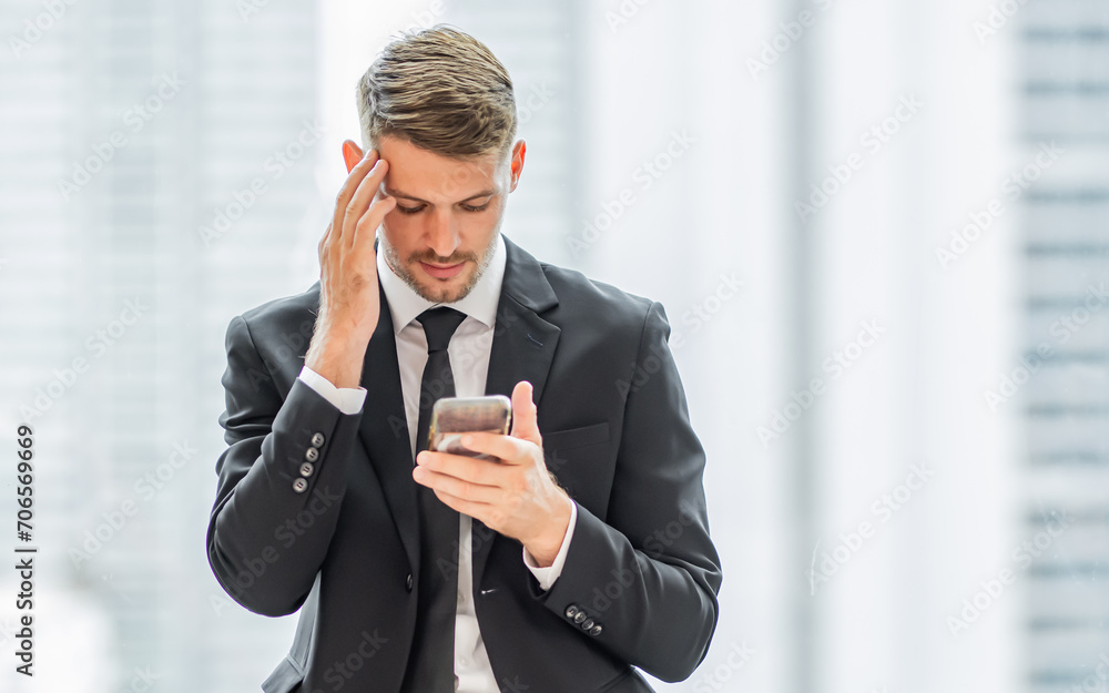 Portrait of handsome Caucasian smart business man wearing formal suit and necktie, serious face, looking at mobile phone with copy space, standing in indoor office. Business Concept. Portrait of handsome Caucasian smart business man wearing formal suit and necktie, serious face, looking at mobile phone with copy space, standing in indoor office. Business Concept.