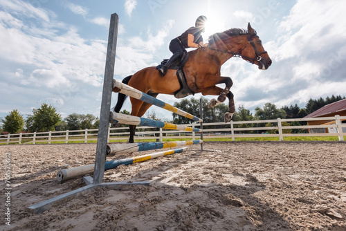 Female horseback rider jumping over a hurdle, a log fence, during training for equestrian competition, low angle view. Art and practice horse riding concept. © 24K-Production