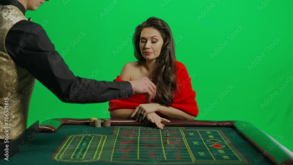 Portrait of attractive female on chroma key green screen. Woman in red dress sitting at the roulette table with croupier, placing bet smiling face. Portrait of attractive female on chroma key green screen. Woman in red dress sitting at the roulette table with croupier, placing bet smiling face.