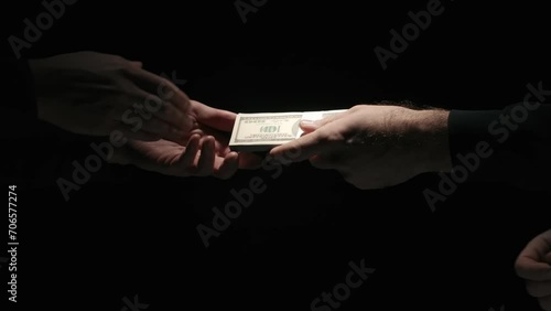 Portrait of business people in suits isolated on black background. Businessman giving wad of banknotes to partner and men making handshake. photo