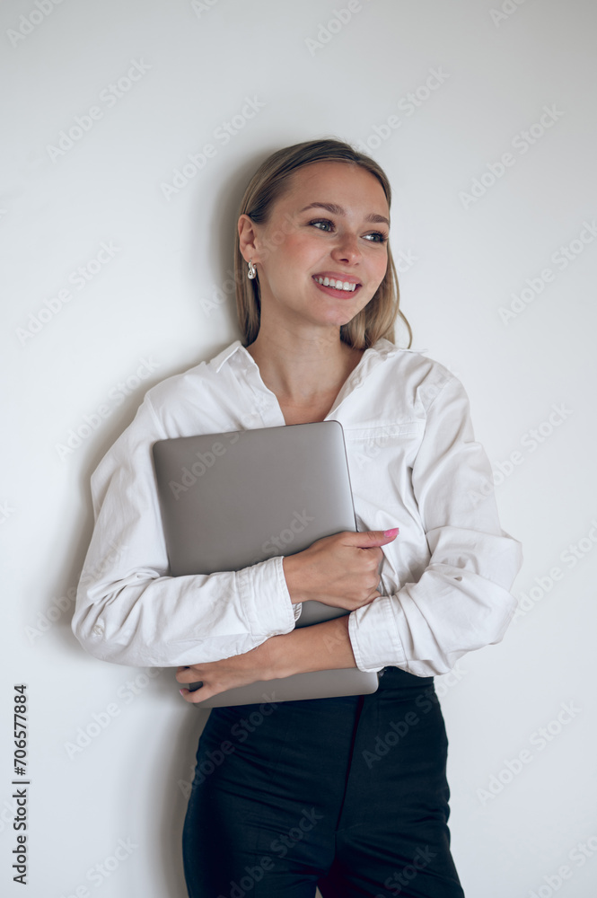 Smiling cute young girl with laptop in hands standing near the wall Smiling cute young girl with laptop in hands standing near the wall