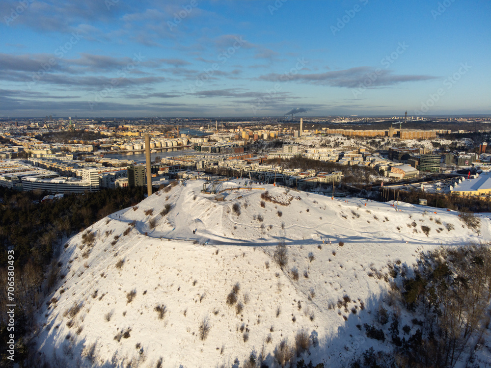  Aerial view of the Stockholm ski slopes at Hammarbybacken, near the district of Hammarby. Downtown stockolm in the background. Partly cloudy, bright light. Snow, winter.