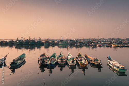 Boats in the harbor tide with the rope where many fishing boats seen behind at the colorful morning sky with perfect reflections at chennai tamilnadu India