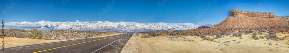 Panoramic picture of a lonely road through desert with snow covered mountains