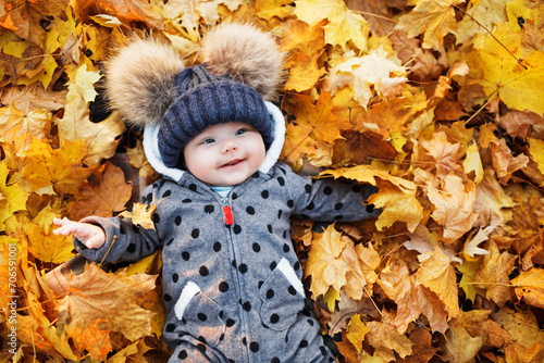 Cute baby lying in autumn leaves.  Smiling baby lying at autumn park with colorful of maple leaves.