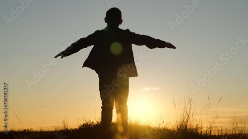 Child boy play like an airplane  in park opposite sky at sunset. Boy aviator dreaming raised his hands to wings of plane on field in rays of sun. Fly concept. Child wants to become an astronaut pilot