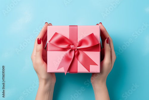 Female hands hold a pink gift box with on the blue background. Background with place for text, copyspace for the holiday, mother's day etc. © Cato_Ri