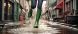 Woman wearing green rubber boots jumps in street puddle.