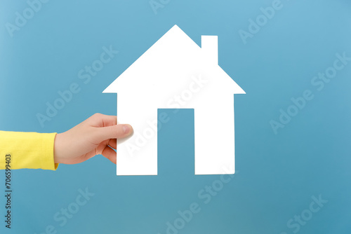 Closeup of female hand holding white paper house  concept of dream home purchase  mortgage  real estate insurance  repairing service concept  posing isolated over blue color background wall in studio