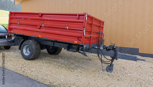 Red trailer with many brake hoses, hydraulic system, wide tires, silver metal locks, hinged loading wall