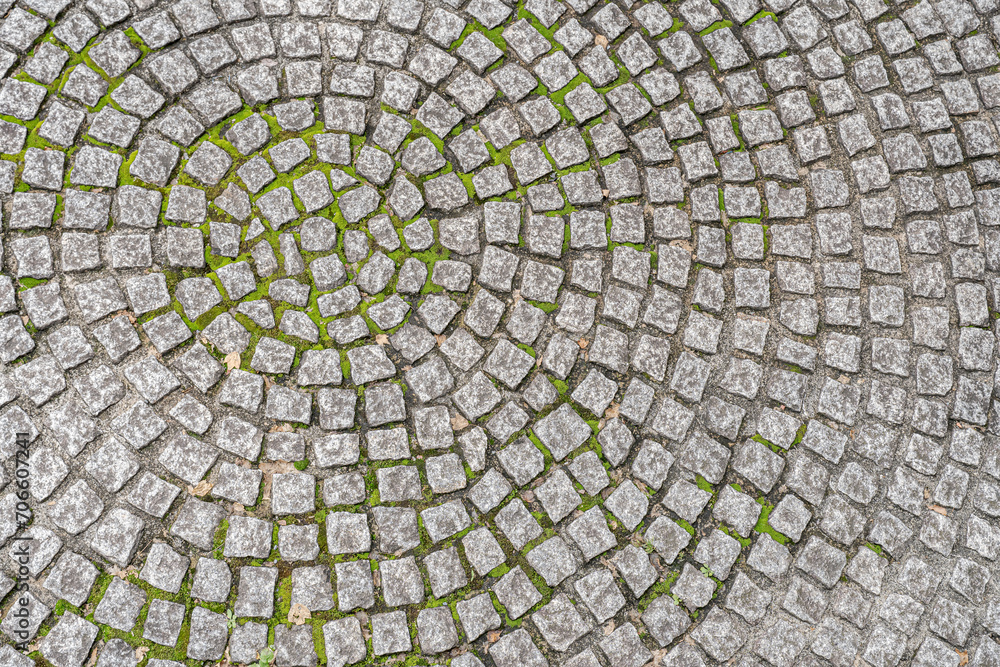 Patio pavers circle design overhead view.
Cut square stones in weathered floor with green moss.