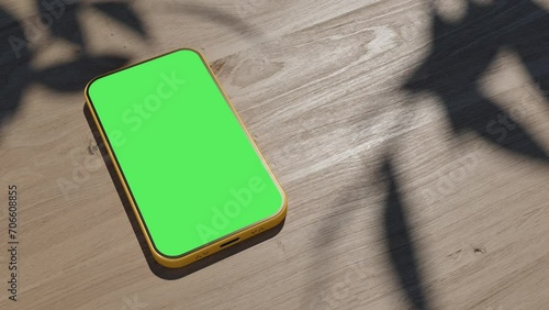 A phone lying on a table, an animation of a gadget on a wooden table. the video has a green screen with shadows from the foliage photo