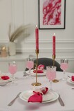 Color accent table setting. Glasses, plates, burning candles and pink napkins on table in dining room