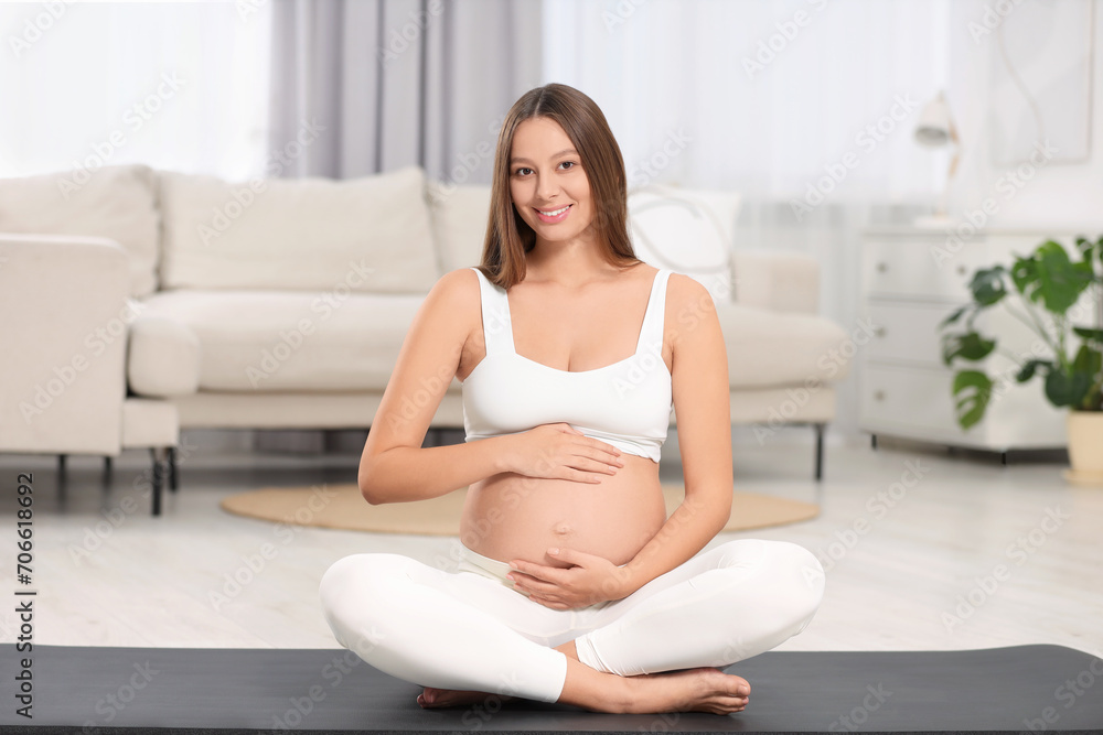 Beautiful pregnant woman sitting on yoga mat at home Beautiful pregnant woman sitting on yoga mat at home
