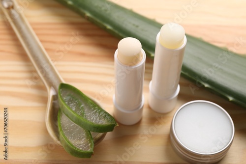 Different lip balms and aloe vera plant on wooden table, closeup