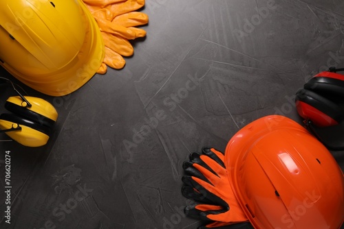 Hard hats, gloves and earmuffs on grey table, flat lay with space for text. Safety equipment