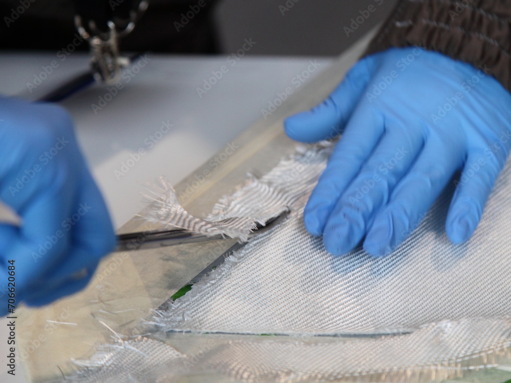 Hands in protective gloves cutting with scissors when Fiberglass products production process of textile fibre glass. Safety when working with fiberglass and epoxy resin