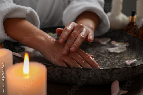 Woman soaking her hands in bowl of water and flower petals  closeup. Spa treatment