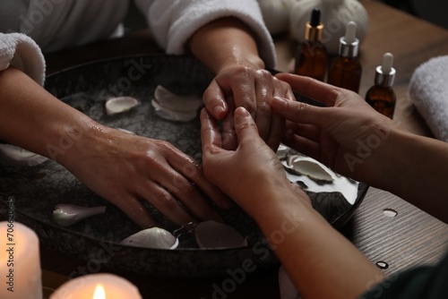 Woman receiving hand massage in spa salon  closeup. Bowl of water and flower petals on table