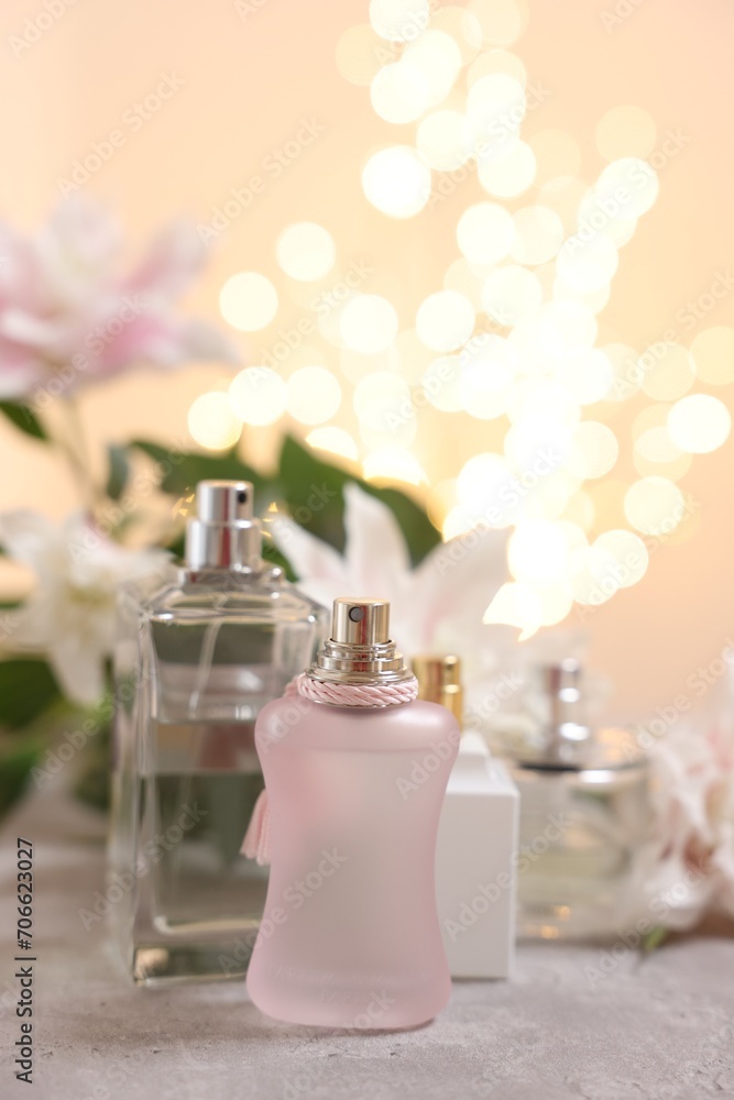 Bottles of perfume on table against beautiful lily flowers and blurred lights, closeup. Space for text Bottles of perfume on table against beautiful lily flowers and blurred lights, closeup. Space for text