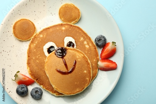 Creative serving for kids. Plate with cute bear made of pancakes and berries on light blue table, top view
