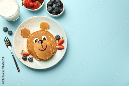 Creative serving for kids. Plate with cute bear made of pancakes and berries on light blue table, flat lay. Space for text