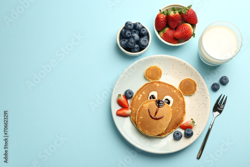Creative serving for kids. Plate with cute bear made of pancakes and berries on light blue table, flat lay. Space for text