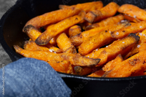 Sweet potato fries cooked in a cast iron frying pan. On a dark stone background